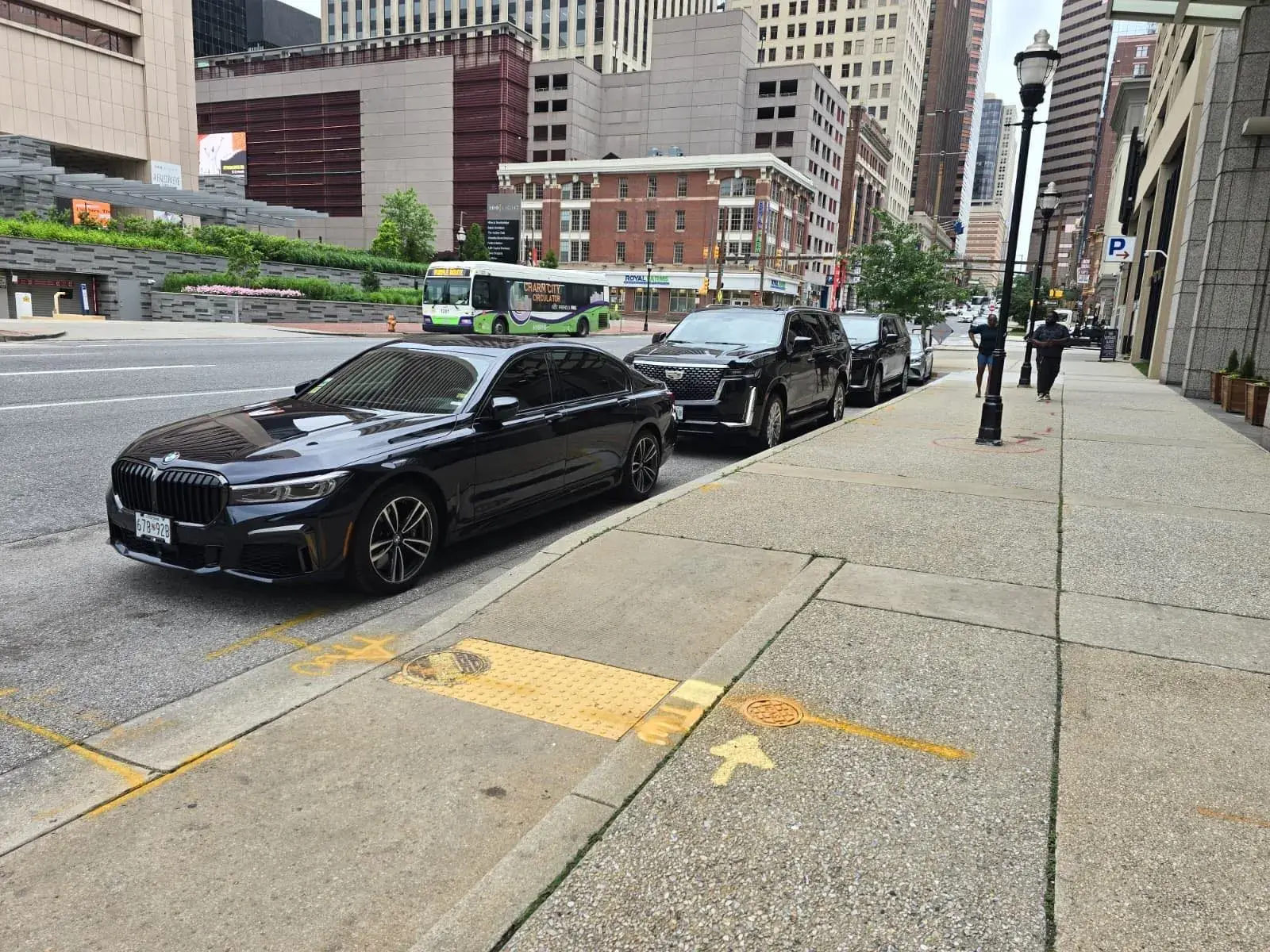 BMW 7 Series and Cadillac Escalade ESV chauffeur vehicles staged curbside in downtown Baltimore